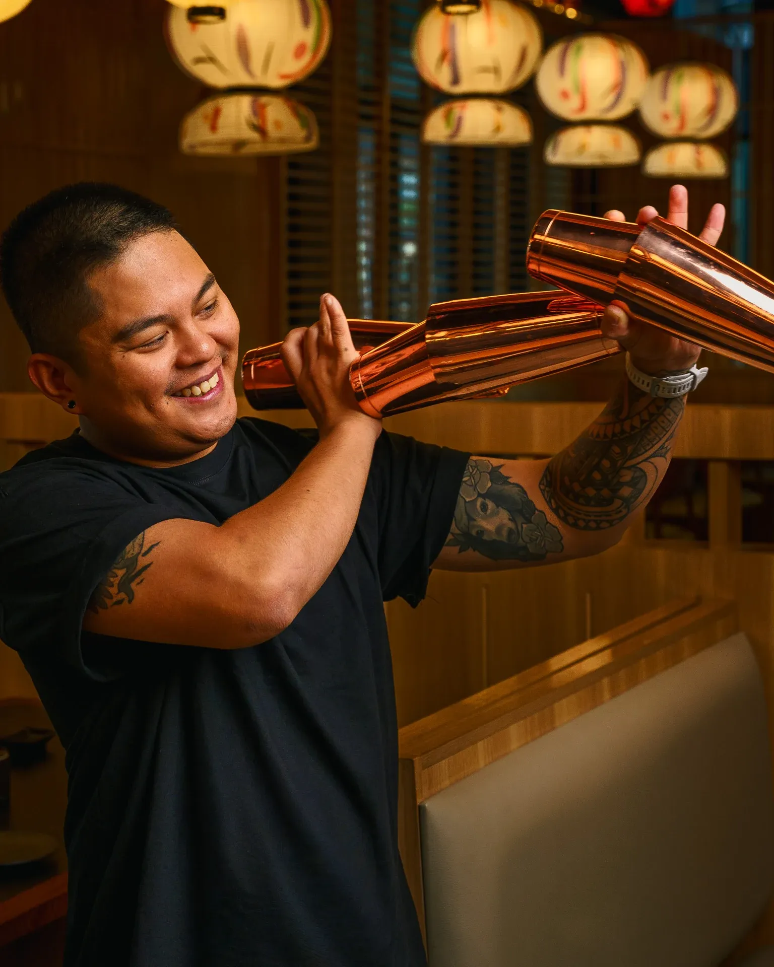 Bartender with interlocked copper cocktail shakers in a warmly lit restaurant