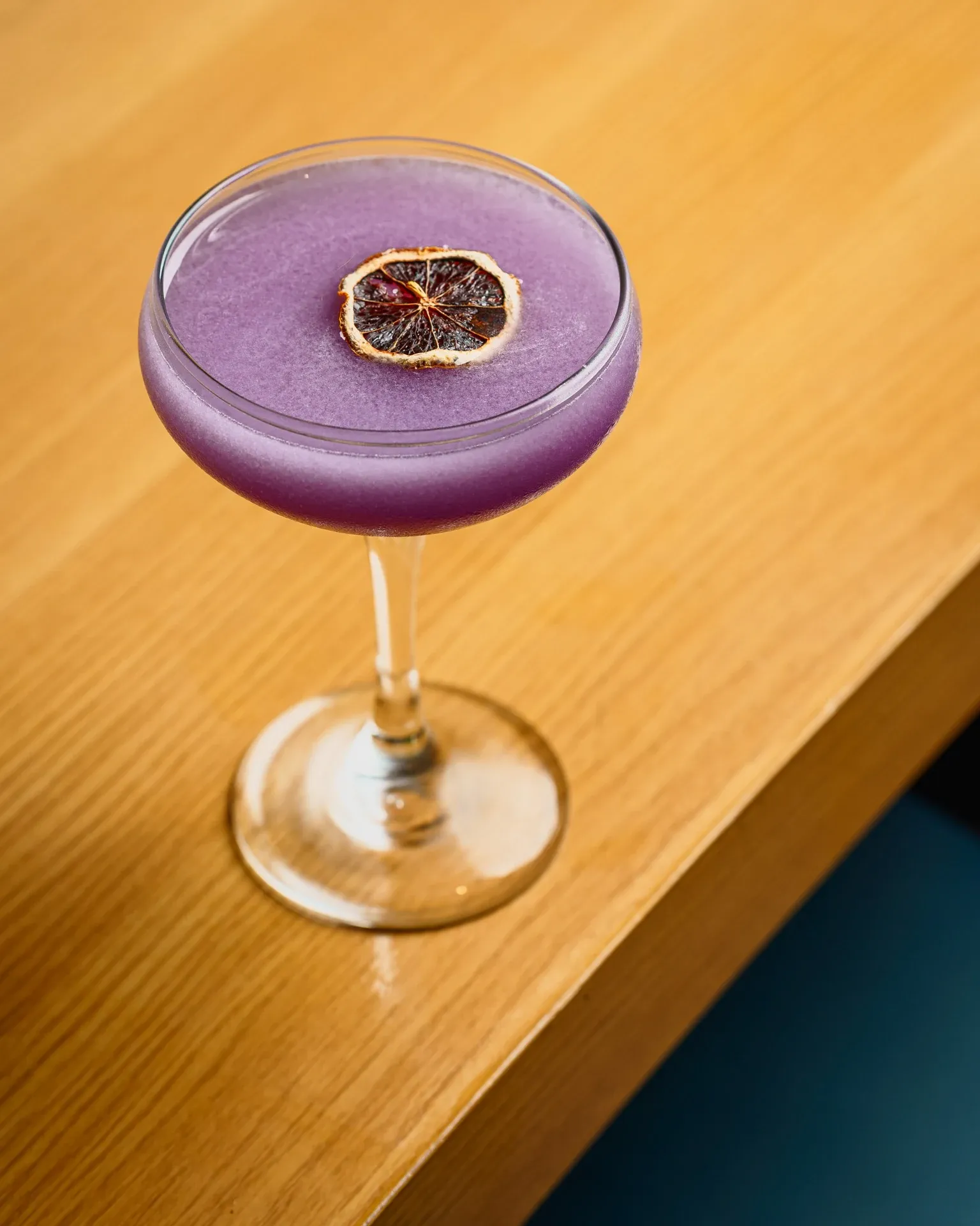 Purple cocktail in a coupe with dried citrus wheel garnish