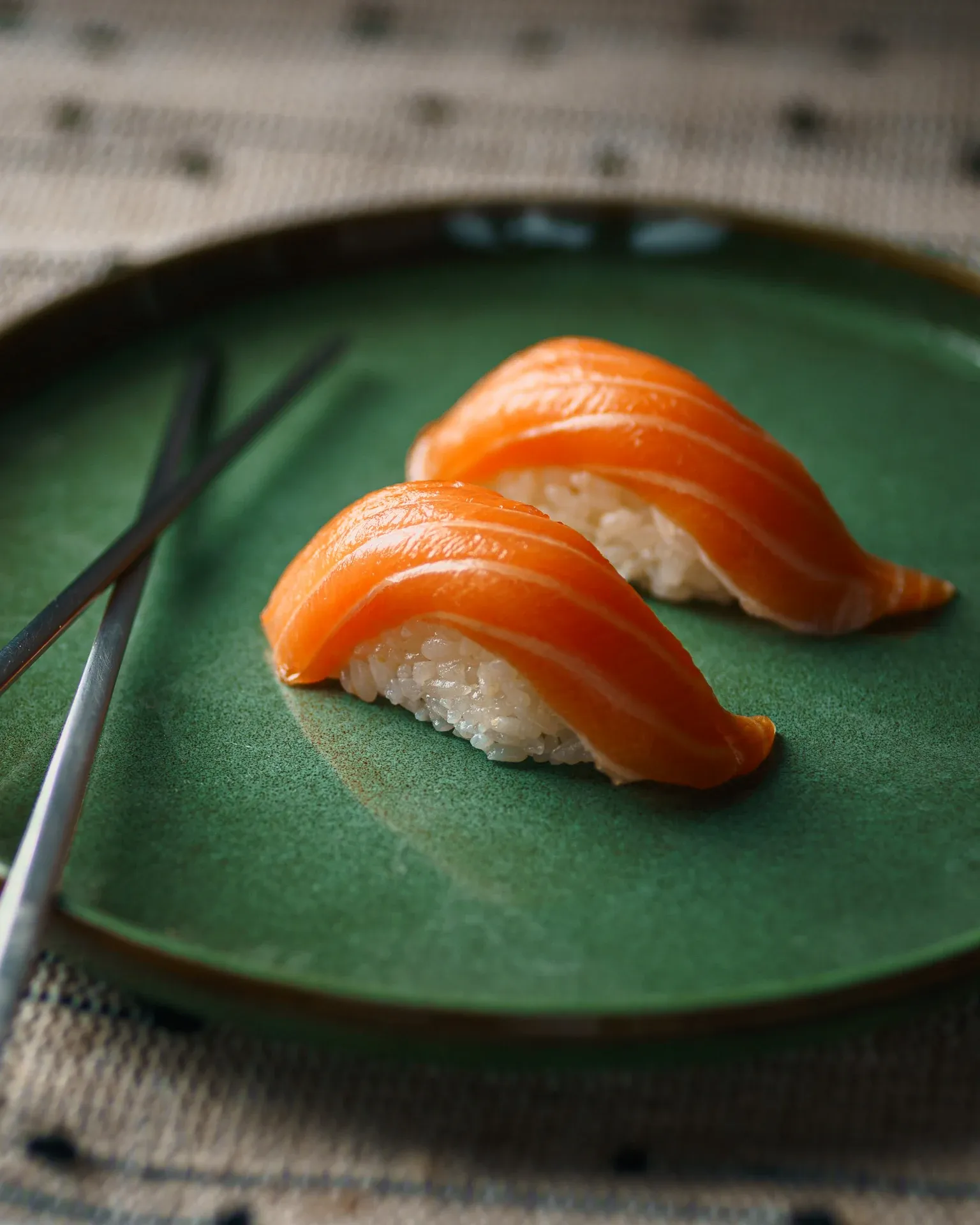 Salmon nigiri on a dark green ceramic plate with chopsticks