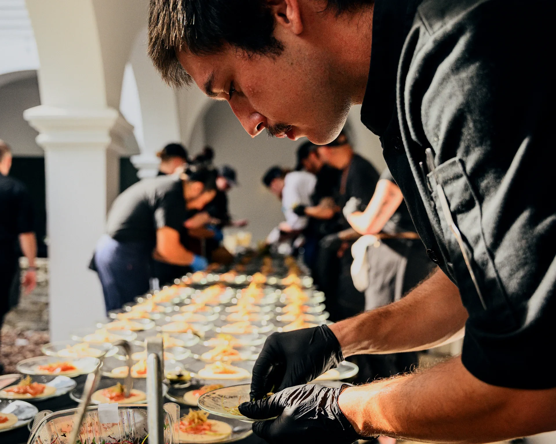 Chef plating rows of hors d'oeuvres for a James Beard dinner under white courtyard arches