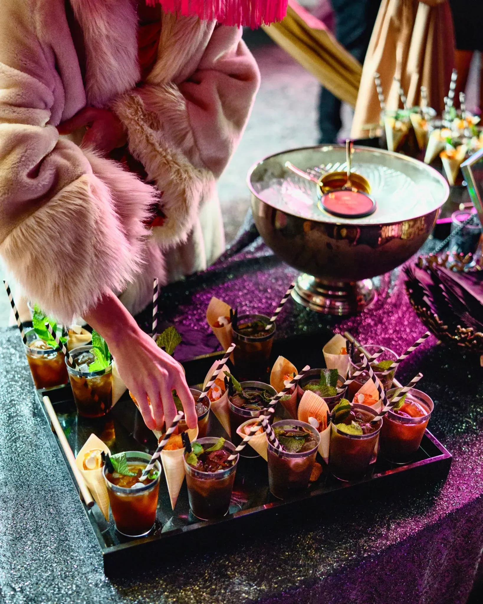 Guest reaching for mint-garnished cocktails from a tray under pink event lighting at the PRI industry event