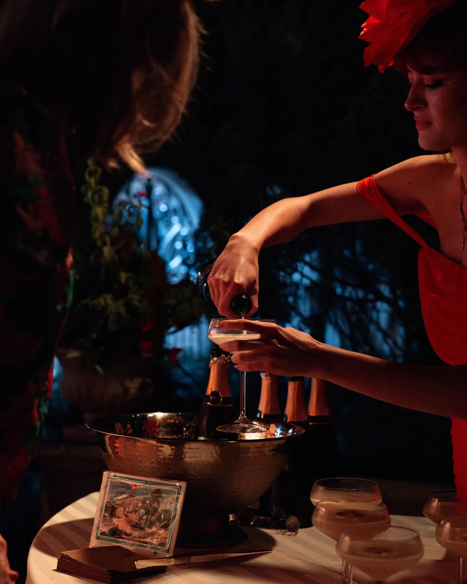 Woman in a red dress and floral headpiece pouring champagne at the San Marco Centennial Soirée